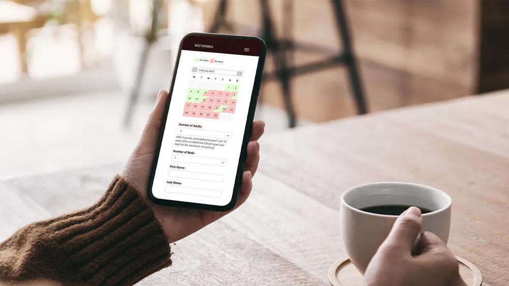 Person holding a phone showing the Rootsprings online booking calendar, part of the custom retreat center website developed by LXE Digital